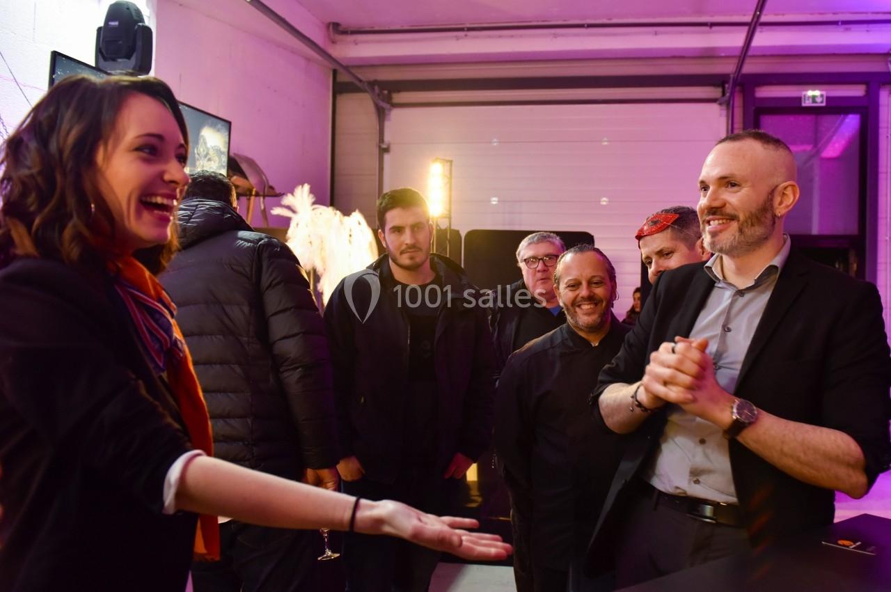 Une femme souriante tend la main à un homme dans un espace intérieur, entourés de plusieurs personnes.