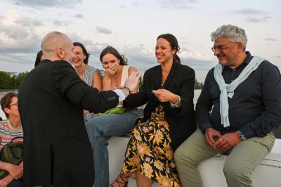 Un groupe de personnes assises et debout, riant et échangeant lors d'un moment convivial en extérieur.