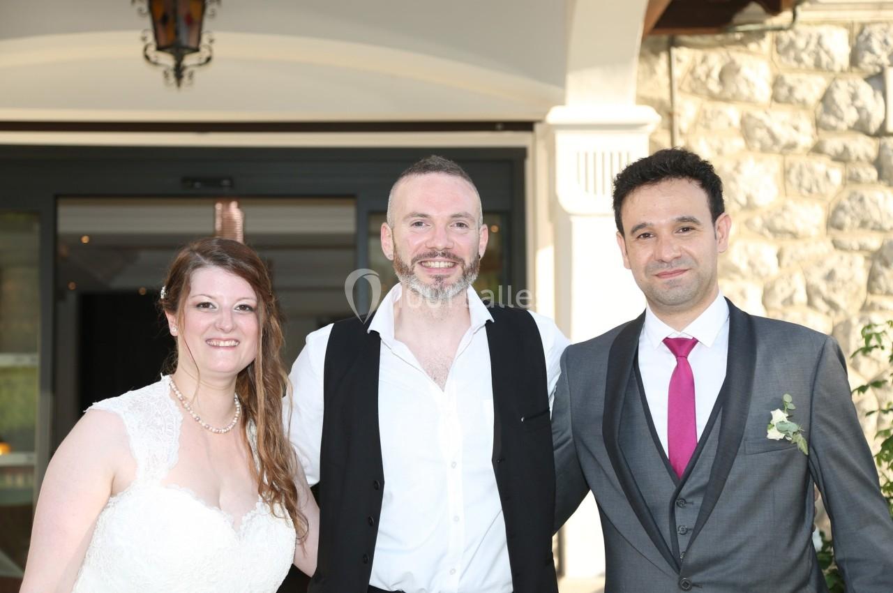 Trois personnes posent ensemble en tenue de mariage devant une entrée de bâtiment en pierre.