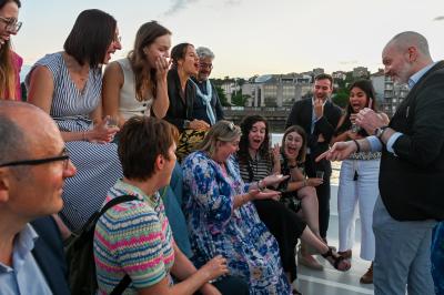 Un groupe de personnes assises et debout, riant et échangeant lors d'un moment convivial en extérieur.