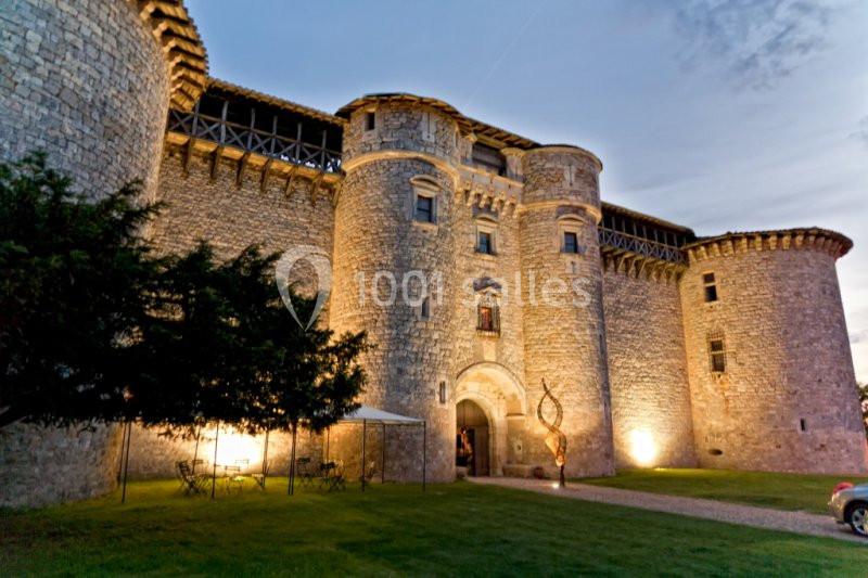 Château en pierre éclairé à la tombée de la nuit, avec une cour herbeuse et des détails architecturaux médiévaux.