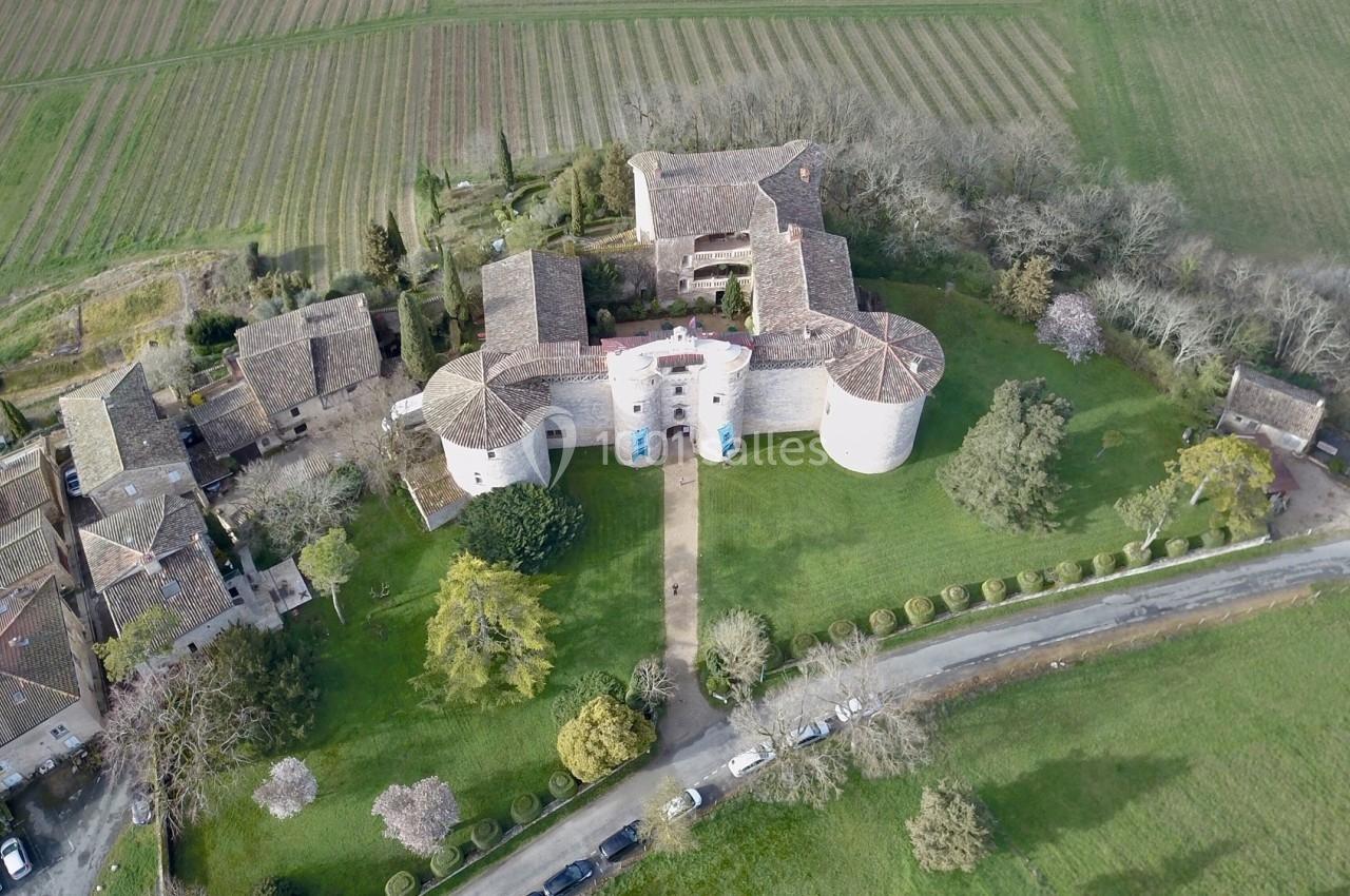 Vue aérienne d'un château entouré de jardins, de bâtiments annexes et de champs verdoyants.