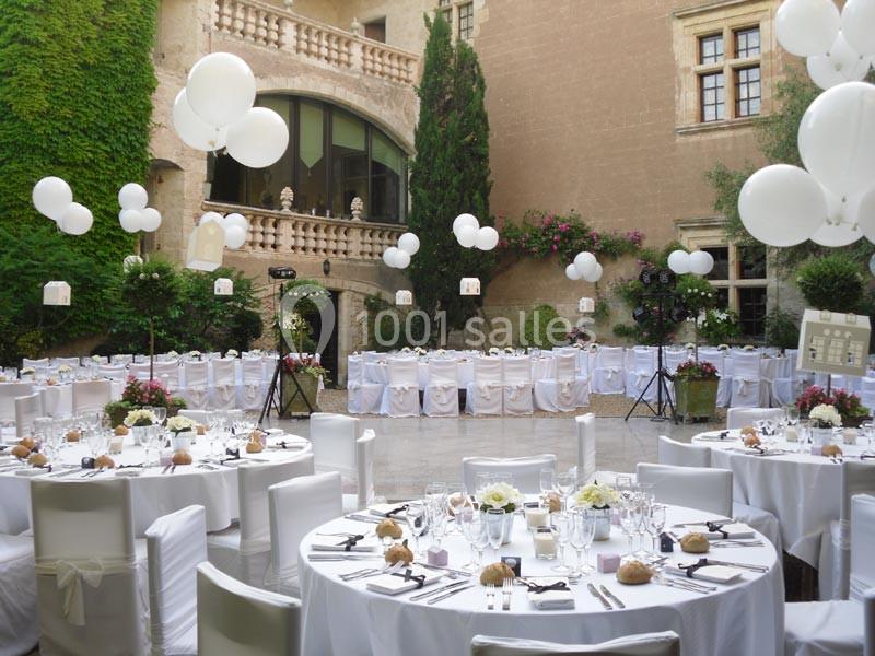 Tables rondes décorées pour un mariage en plein air dans une cour avec ballons blancs et végétation murale.