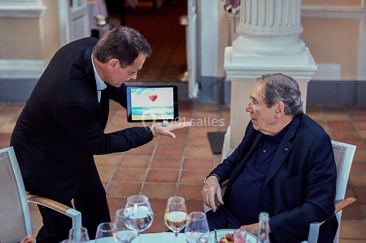 Un serveur montre une tablette avec une image de cœur à un homme assis à une table dans un restaurant élégant.
