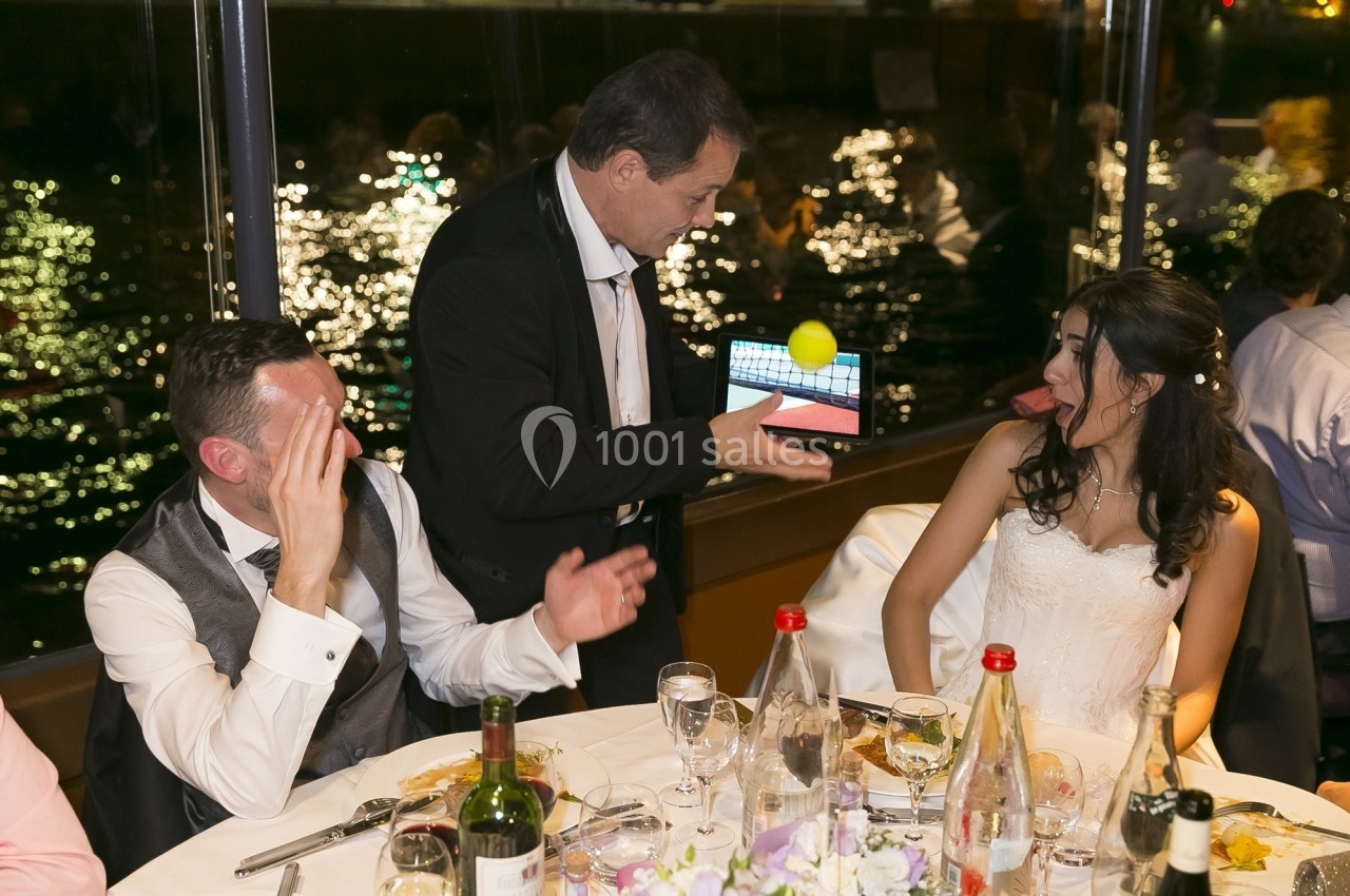 Un magicien montre un tour avec une balle et une tablette à des convives assis à une table lors d'un dîner.