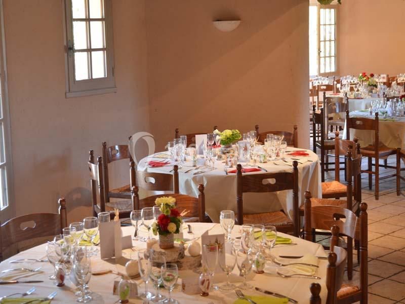 Salle de réception avec tables rondes dressées, nappes blanches, verres, couverts et décorations florales.