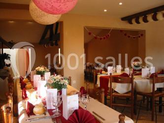 Salle de réception décorée avec des tables dressées, nappes rouges, fleurs et guirlandes suspendues.