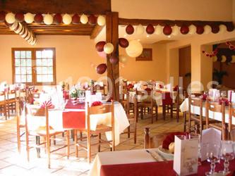Salle de réception décorée avec des tables dressées, nappes rouges et blanches, et guirlandes suspendues.