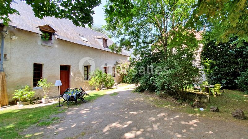Cour ombragée avec maison en pierre, mobilier de jardin et végétation abondante sous un ciel dégagé.