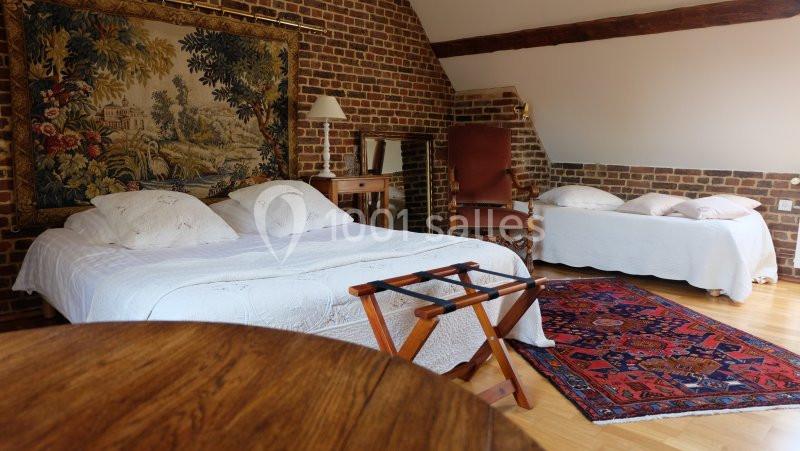 Chambre avec murs en briques, lit double, lit simple, tapis coloré et mobilier en bois dans un décor rustique.
