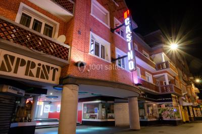 Entrée éclairée d'un casino avec enseigne lumineuse, sol coloré et portes vitrées donnant sur l'intérieur.