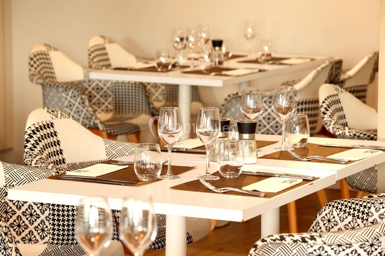 Salle de restaurant avec tables dressées, nappes blanches, verres, assiettes et chaises au motif géométrique.