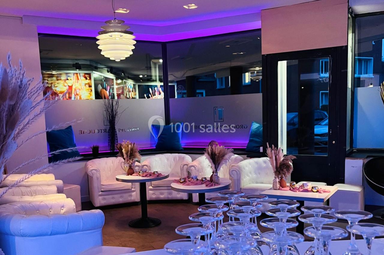 Salon moderne avec canapés blancs, tables décorées de fleurs séchées, éclairage violet et grandes fenêtres donnant sur la…