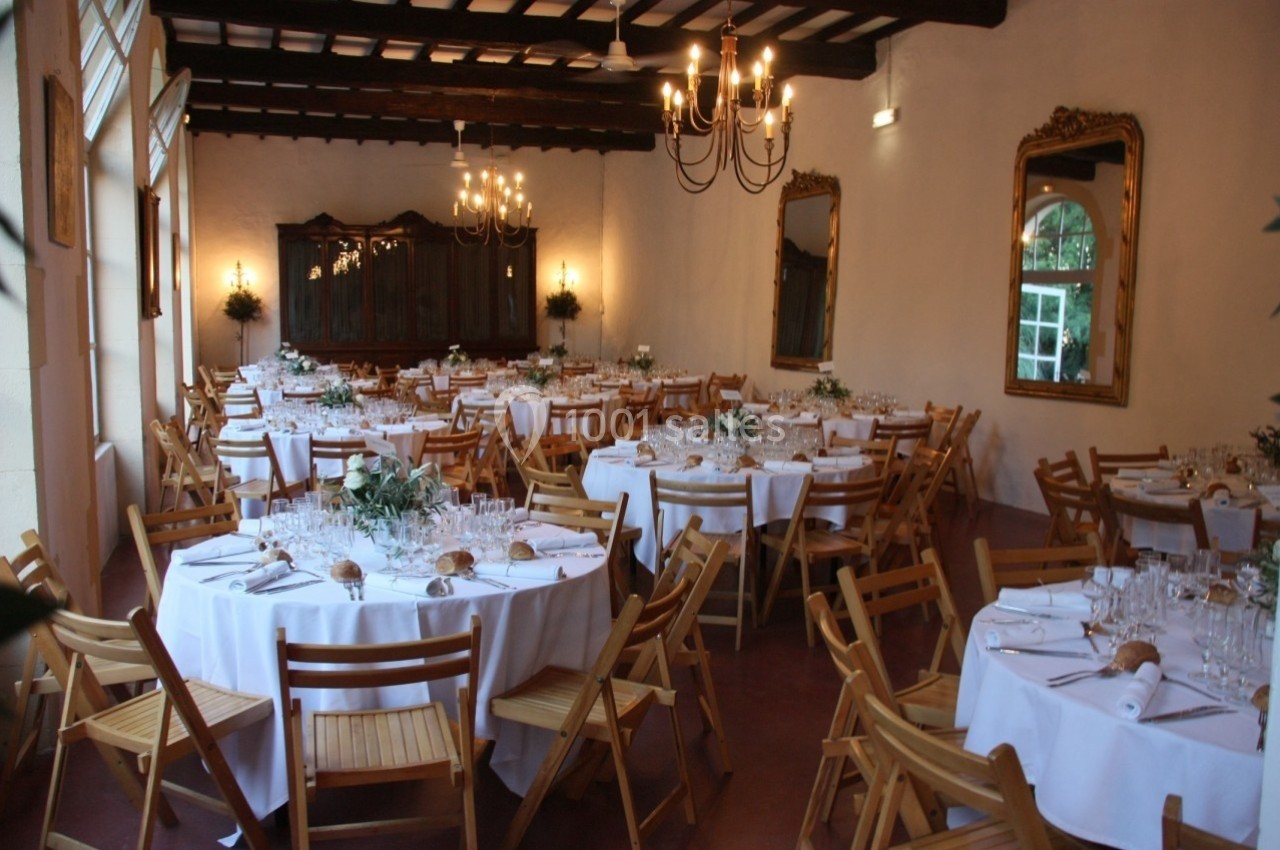 Salle de réception élégante avec tables rondes dressées, chaises en bois, miroirs et lustres suspendus.