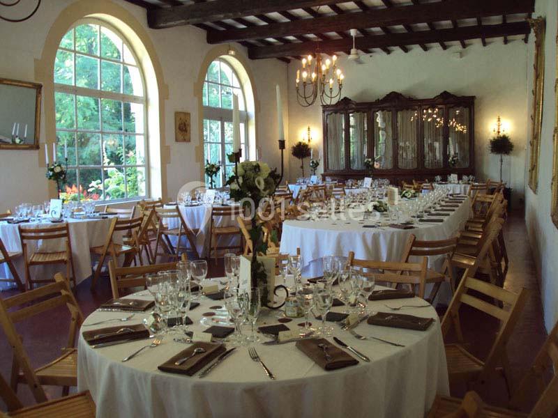 Salle de réception élégante avec tables rondes dressées, chaises en bois et grandes fenêtres laissant entrer la lumière…
