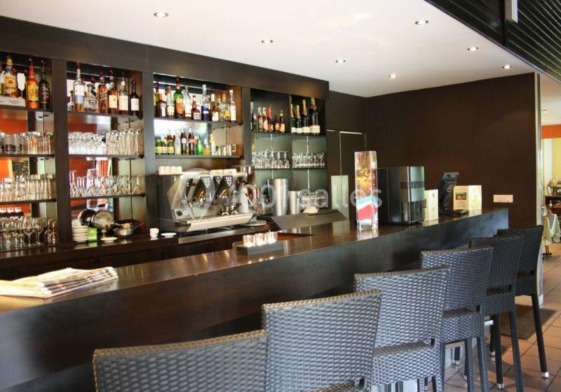 Comptoir de bar moderne avec tabourets en osier, étagères garnies de bouteilles et machine à café en arrière-plan.