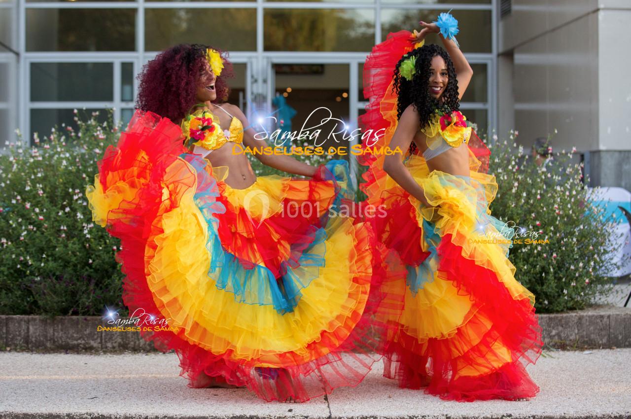 Deux danseuses en tenue colorée de samba exécutent une performance devant un bâtiment moderne.