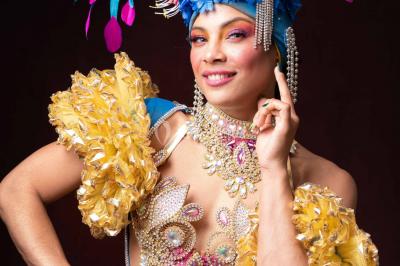 Trois hommes souriants en tenue de capoeira avec des drapeaux brésiliens, posant dans un parc ensoleillé.