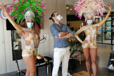 Trois hommes souriants en tenue de capoeira avec des drapeaux brésiliens, posant dans un parc ensoleillé.