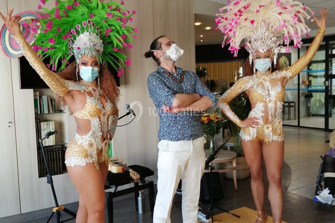 Deux danseuses en costumes à plumes colorées posent avec un homme masqué dans un espace intérieur.