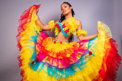 Trois hommes souriants en tenue de capoeira avec des drapeaux brésiliens, posant dans un parc ensoleillé.
