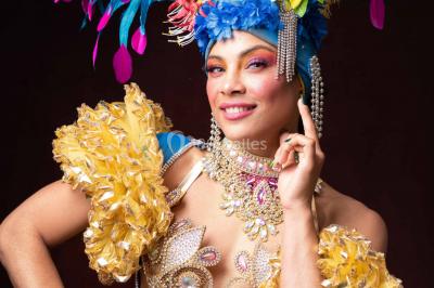 Trois hommes souriants en tenue de capoeira avec des drapeaux brésiliens, posant dans un parc ensoleillé.