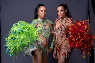 Trois hommes souriants en tenue de capoeira avec des drapeaux brésiliens, posant dans un parc ensoleillé.