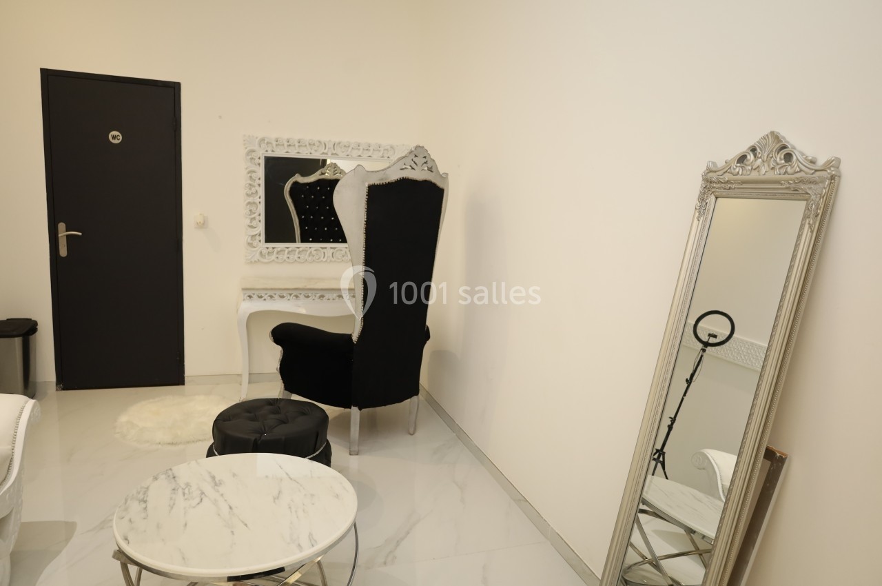 Salle lumineuse avec fauteuil noir, coiffeuse blanche, miroir sur pied et table basse ronde en marbre.