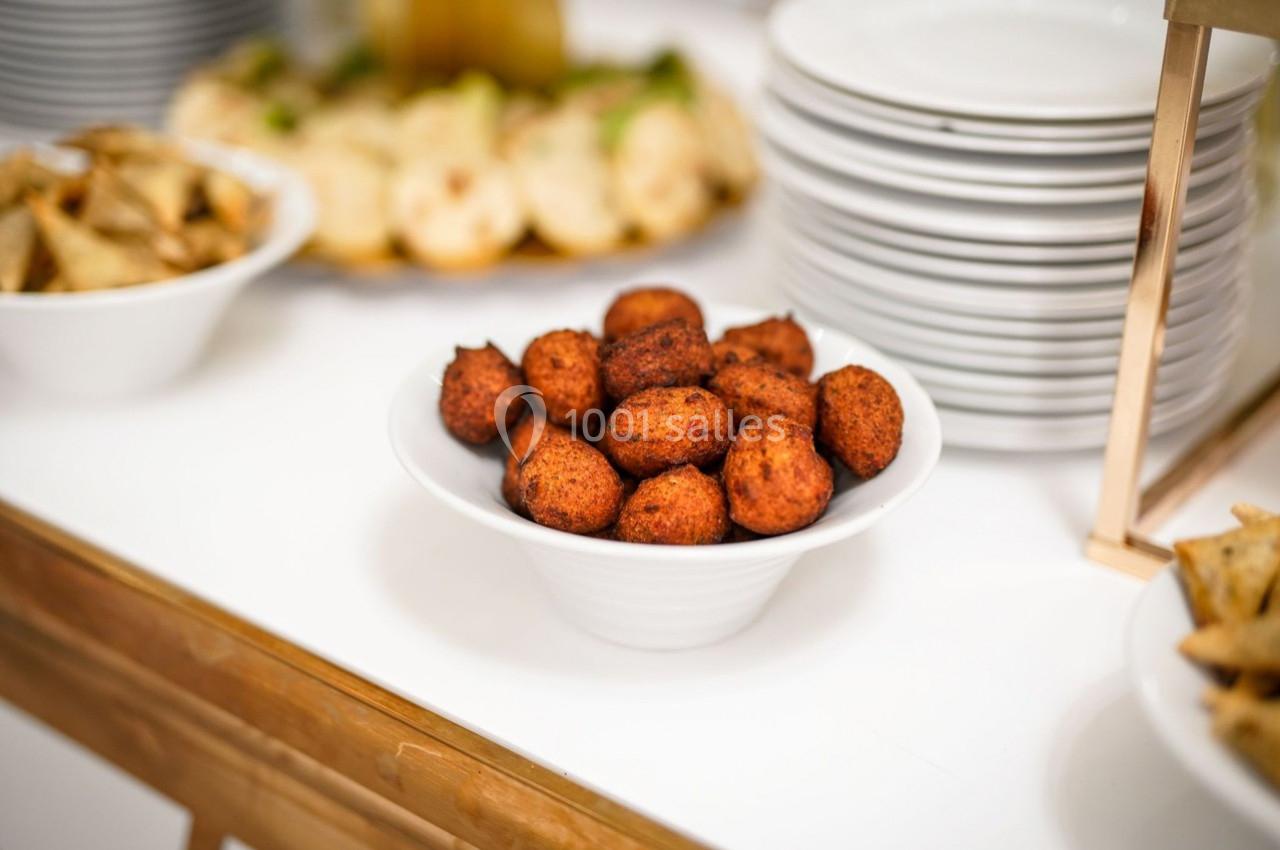 Bol de beignets dorés sur une table, entouré d'assiettes empilées et d'autres plats.