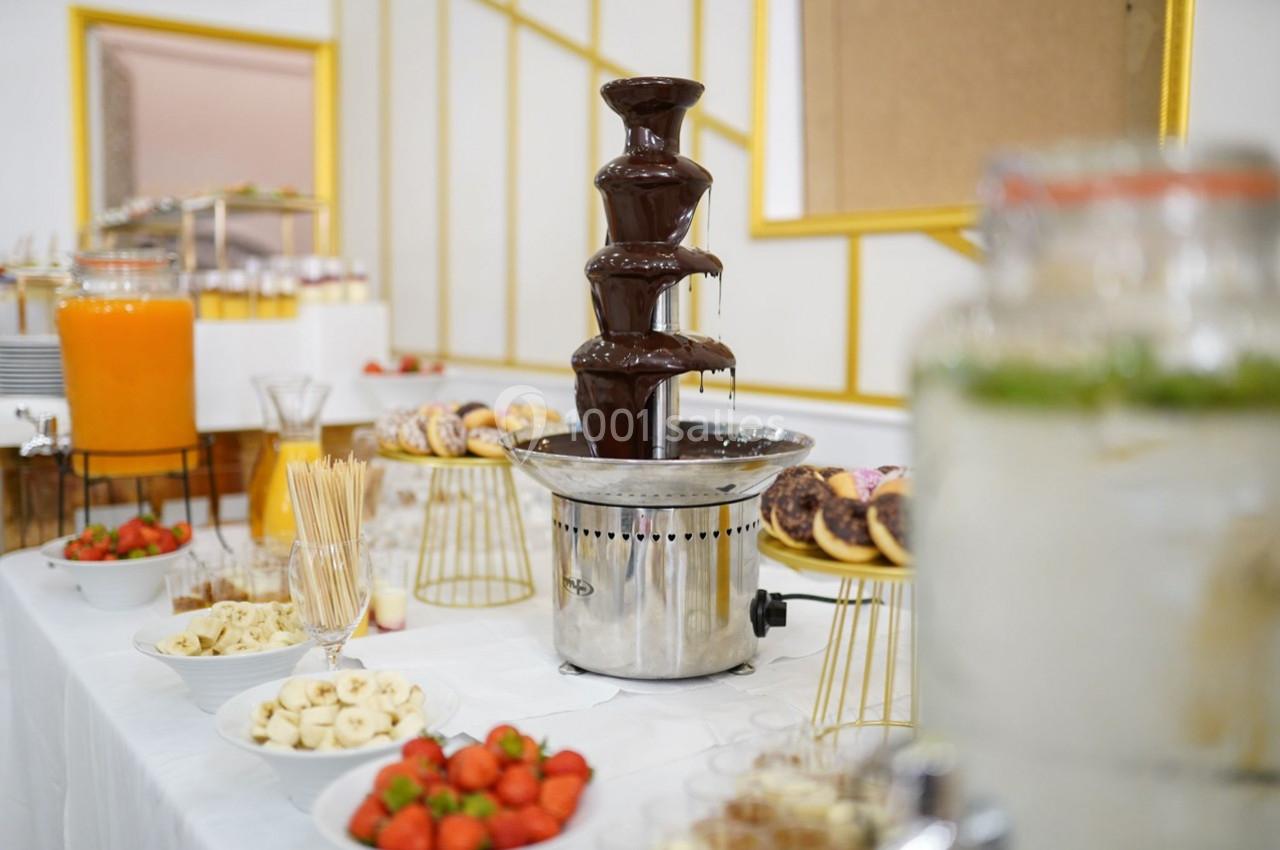 Fontaine à chocolat entourée de fruits frais, brochettes et pâtisseries sur une table de buffet.