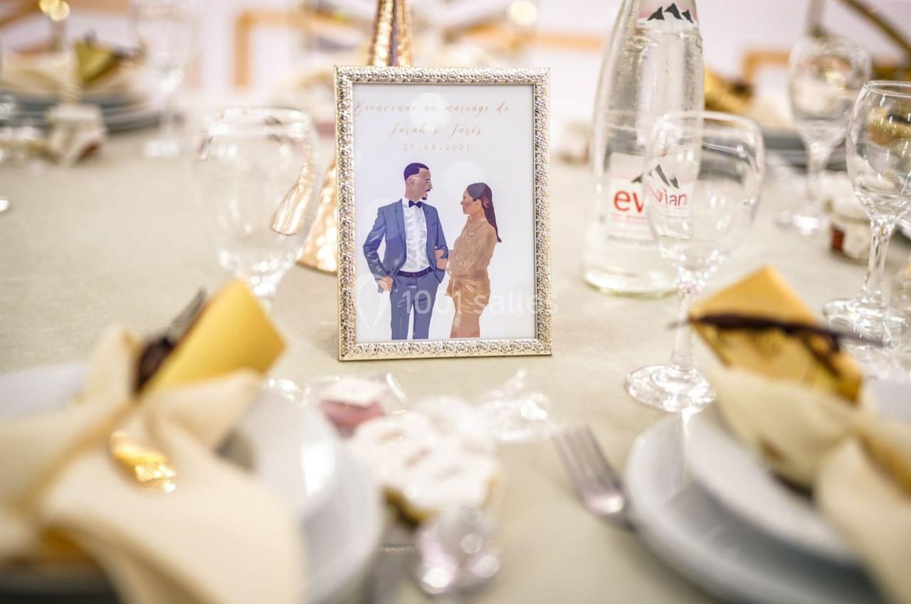 Cadre photo d'un couple posé sur une table de réception décorée avec des assiettes, verres et serviettes pliées.