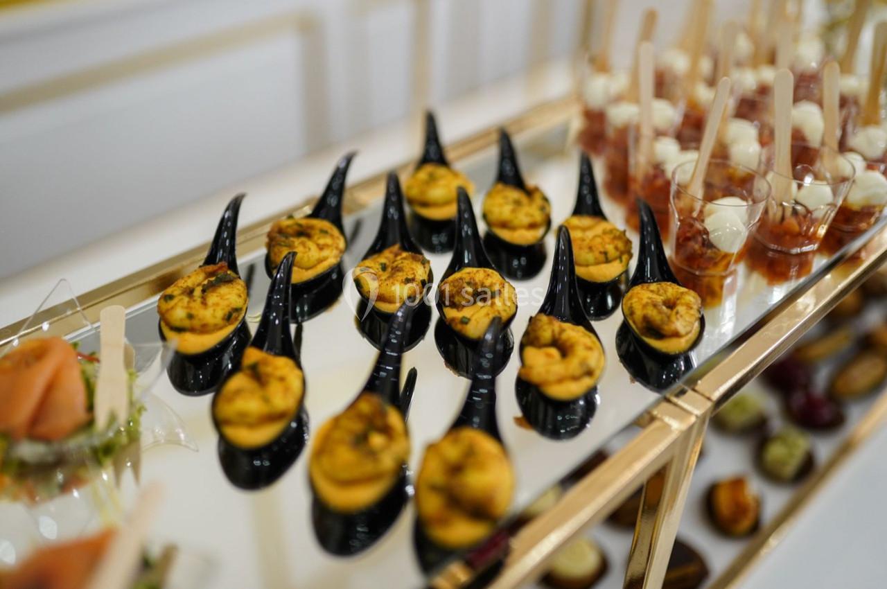 Plateau de bouchées apéritives variées, comprenant des mini-quiches sur cuillères noires et des verrines en arrière-plan.