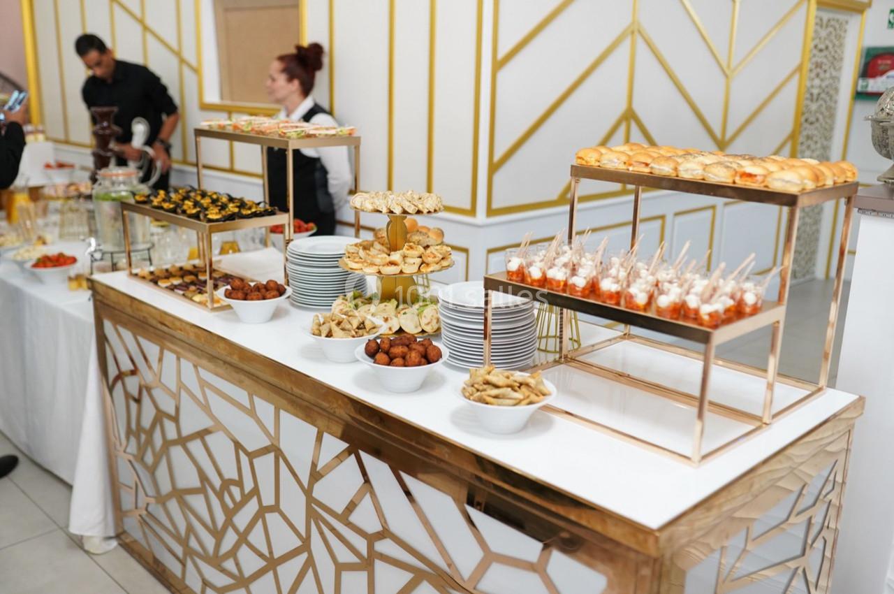 Buffet avec divers amuse-bouches, verrines, et petits pains disposés sur des présentoirs dorés dans un cadre élégant.