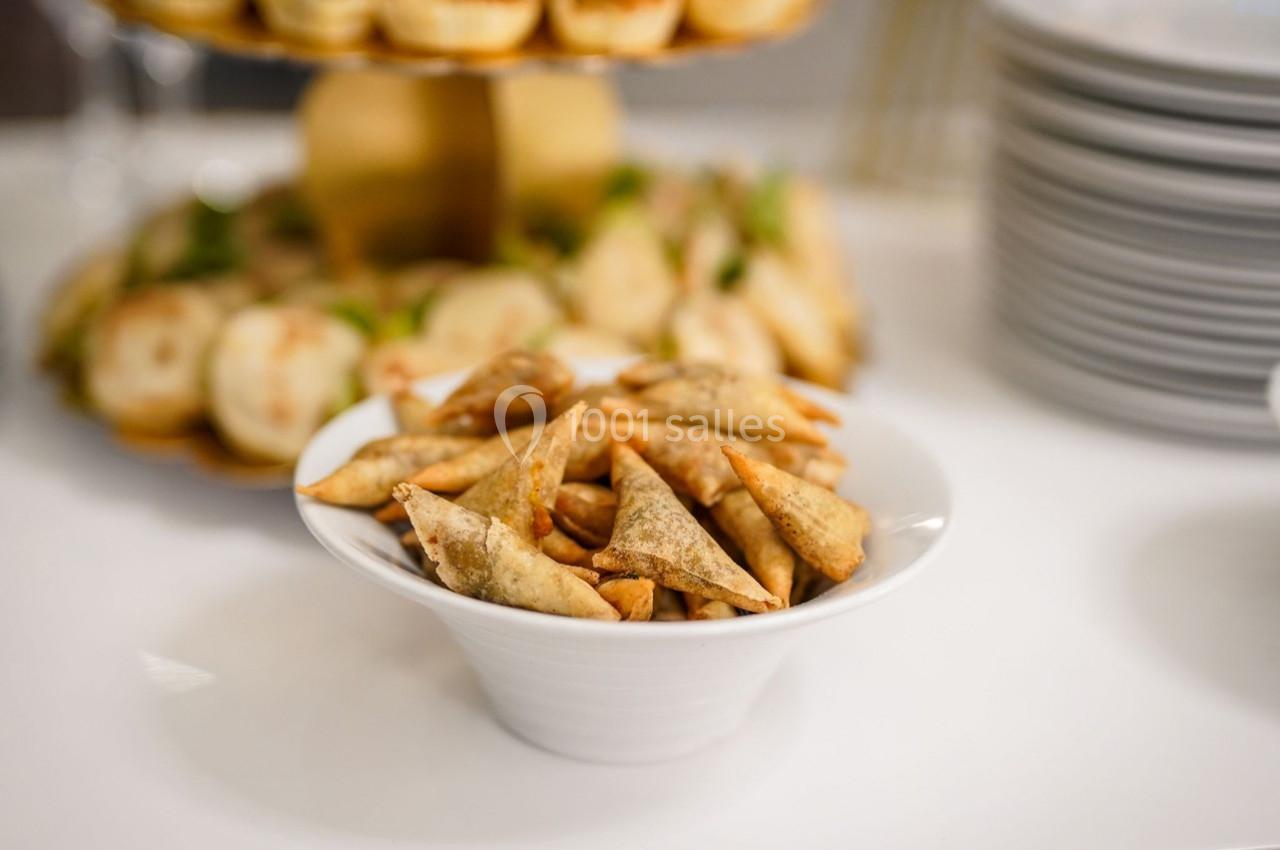 Assiette blanche contenant des samoussas dorés, posée sur une table avec d'autres plats flous en arrière-plan.