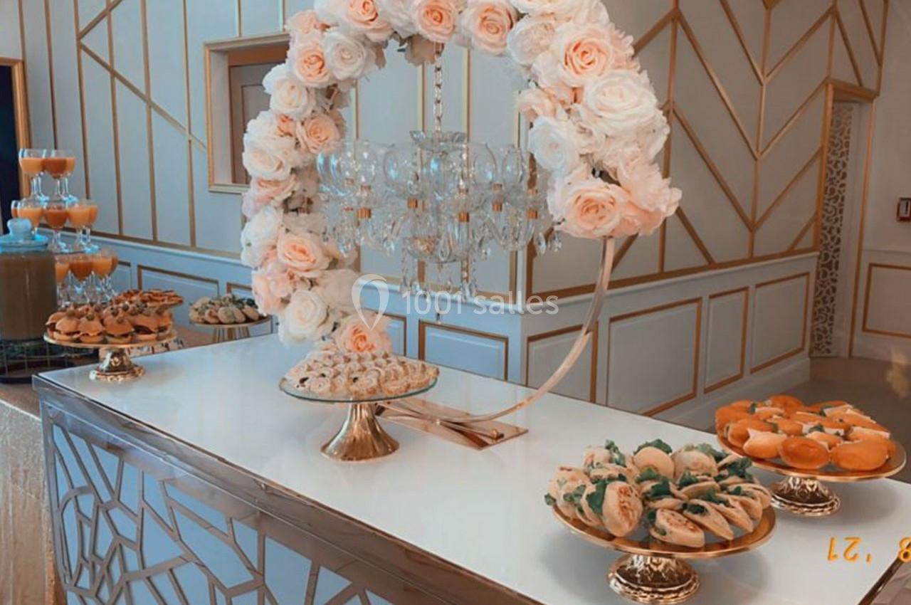Table décorée avec des fleurs et un lustre, présentant des plateaux de pâtisseries variées dans un cadre élégant.