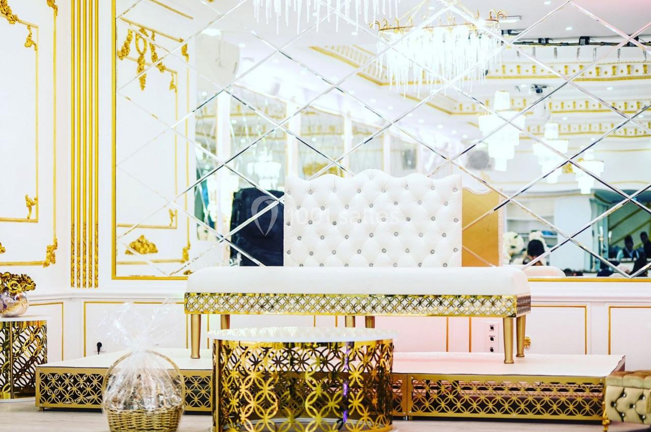 Salle décorée avec des motifs dorés, un banc capitonné blanc et des miroirs en arrière-plan.