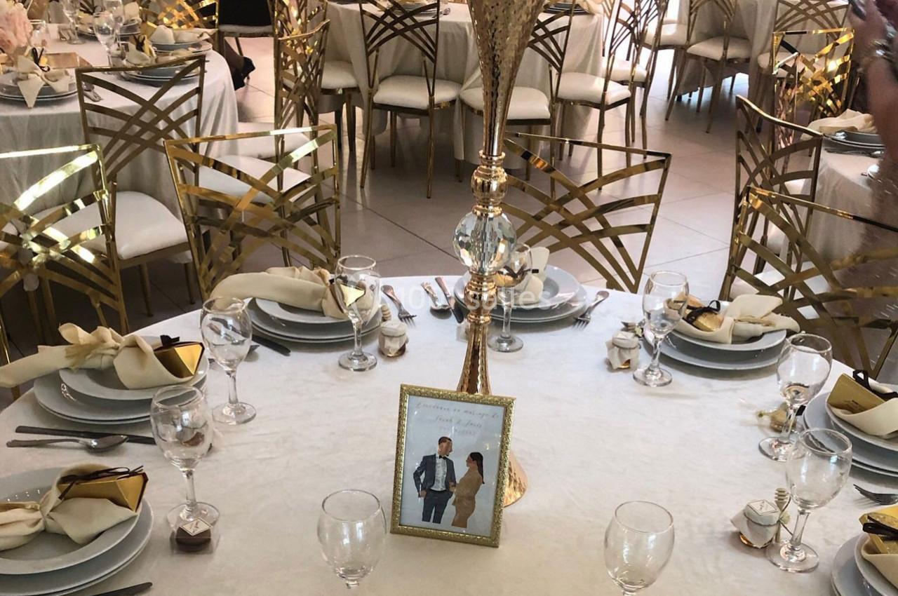Table élégamment dressée avec nappes blanches, vaisselle raffinée, serviettes pliées et centre de table doré.