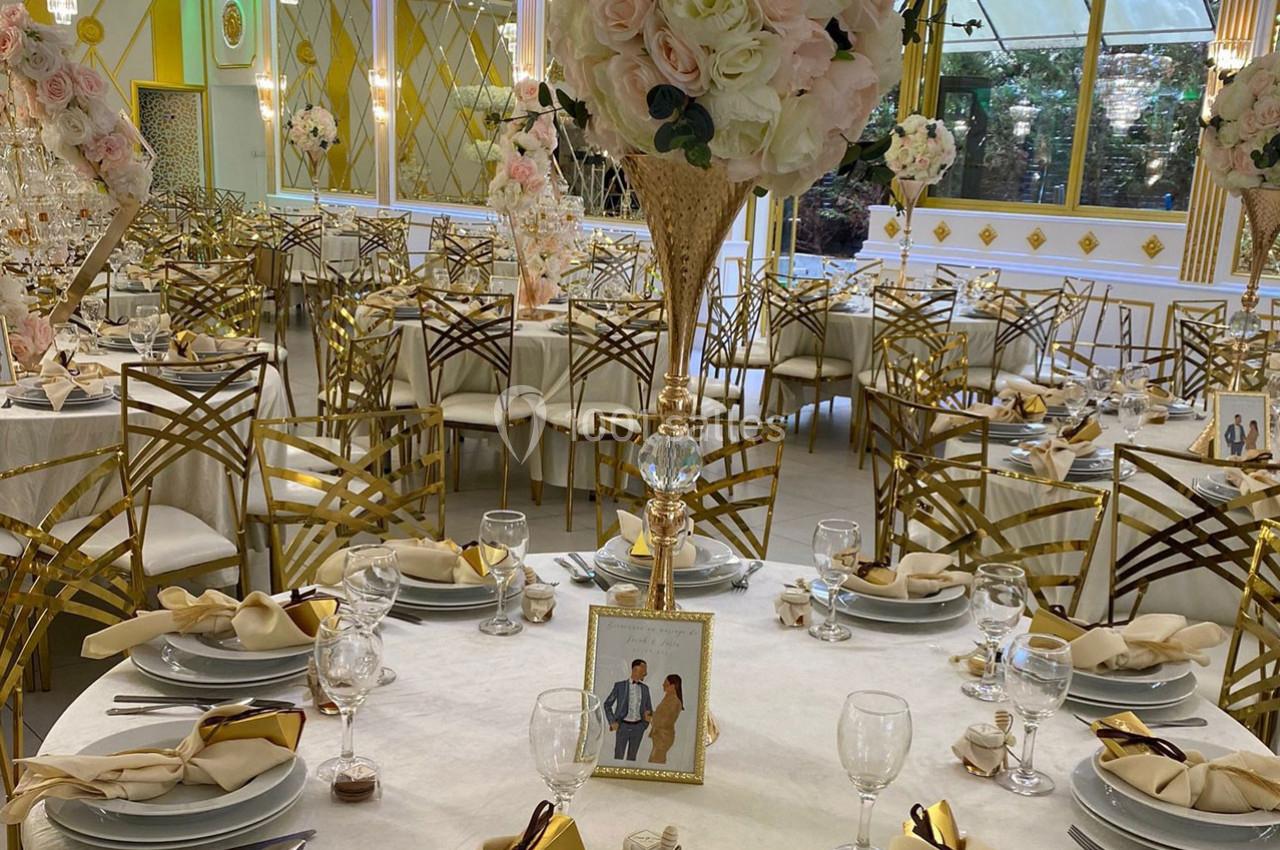 Salle de réception élégante avec tables dressées, décorations florales et chaises dorées au design raffiné.