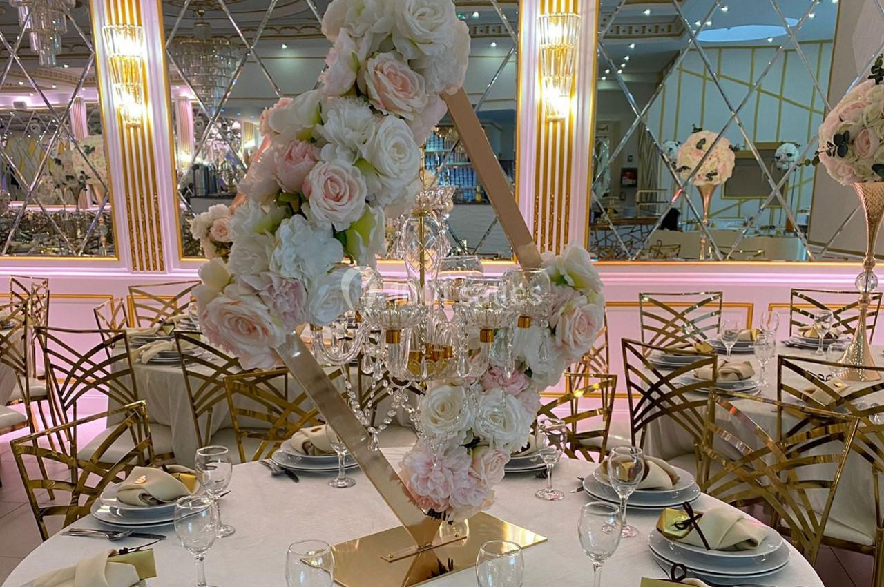 Centre de table floral avec roses blanches et roses, disposé autour d'un chandelier doré sur une table élégamment dressée.
