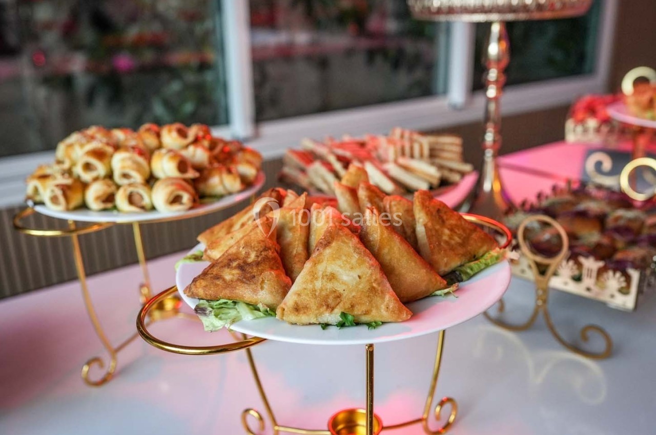 Assortiment de samoussas, feuilletés et sandwichs présentés sur des plateaux dorés dans un cadre lumineux.
