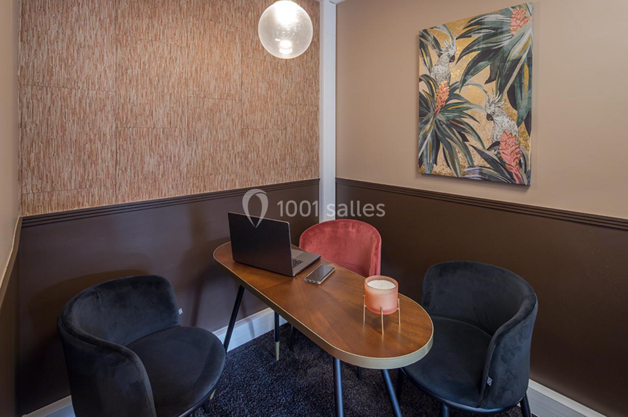 Salle de réunion compacte avec table ovale, chaises colorées, ordinateur portable et tableau décoratif au mur.