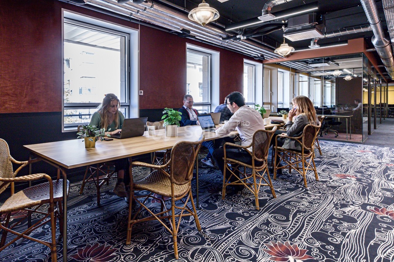 Personnes travaillant sur des ordinateurs portables autour d'une grande table dans un espace de coworking lumineux et décoré.