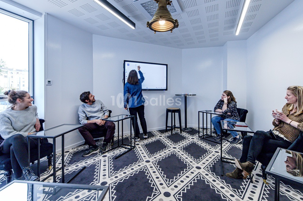 Quatre personnes assises et une debout devant un écran interactif dans une salle de réunion lumineuse.
