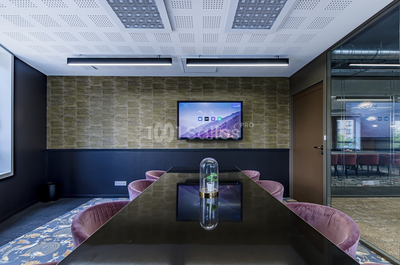 Salle de réunion moderne avec table noire, chaises violettes, écran mural et grande fenêtre laissant entrer la lumière…