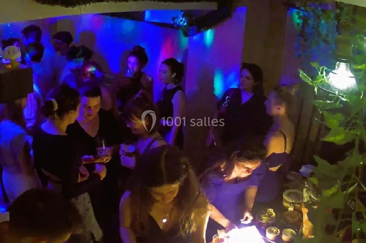 Personnes rassemblées dans un espace intérieur faiblement éclairé, avec des lumières colorées et une ambiance festive.