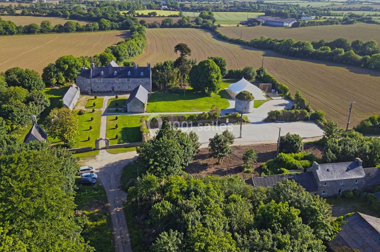 Vue aérienne d'un domaine rural avec bâtiments en pierre, jardin aménagé, moulin et champs environnants.