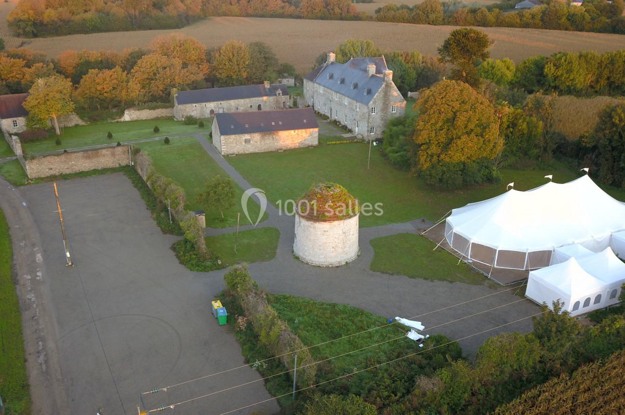 Vue aérienne d'un domaine rural avec bâtiments en pierre, une tente blanche et des espaces verts environnants.