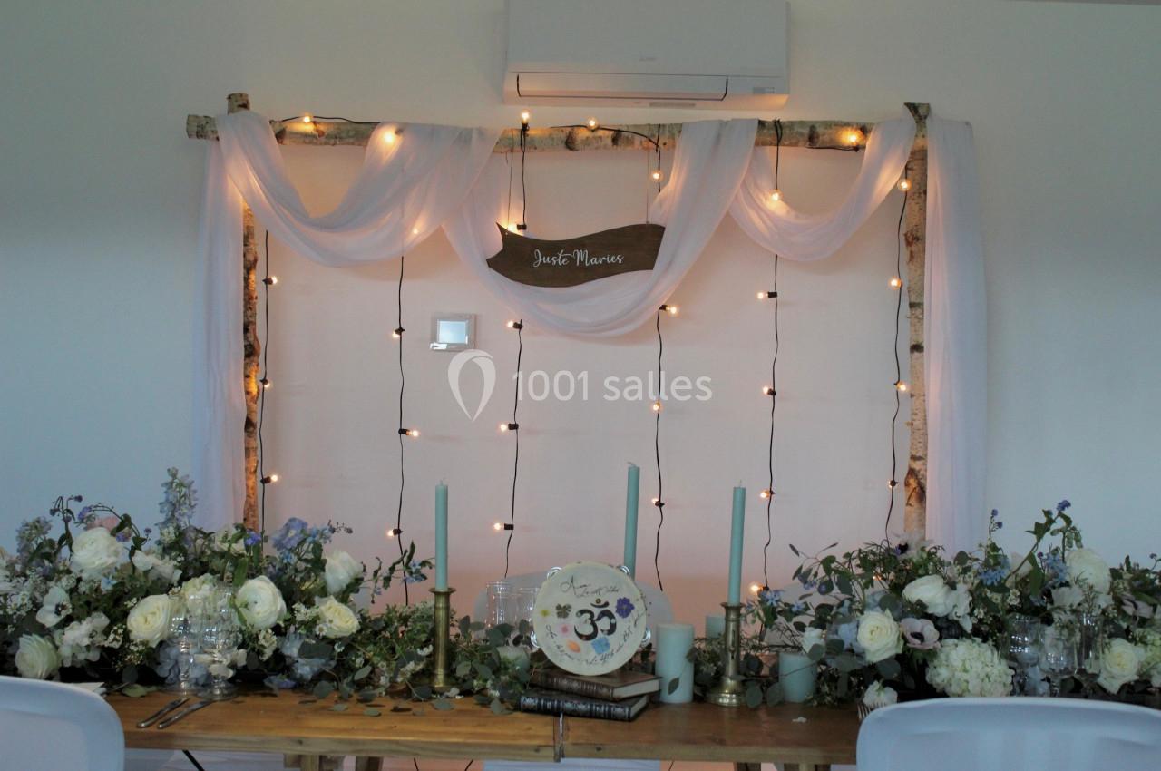 Décoration de table de mariage avec fleurs blanches, bougies, guirlandes lumineuses et drapés suspendus.