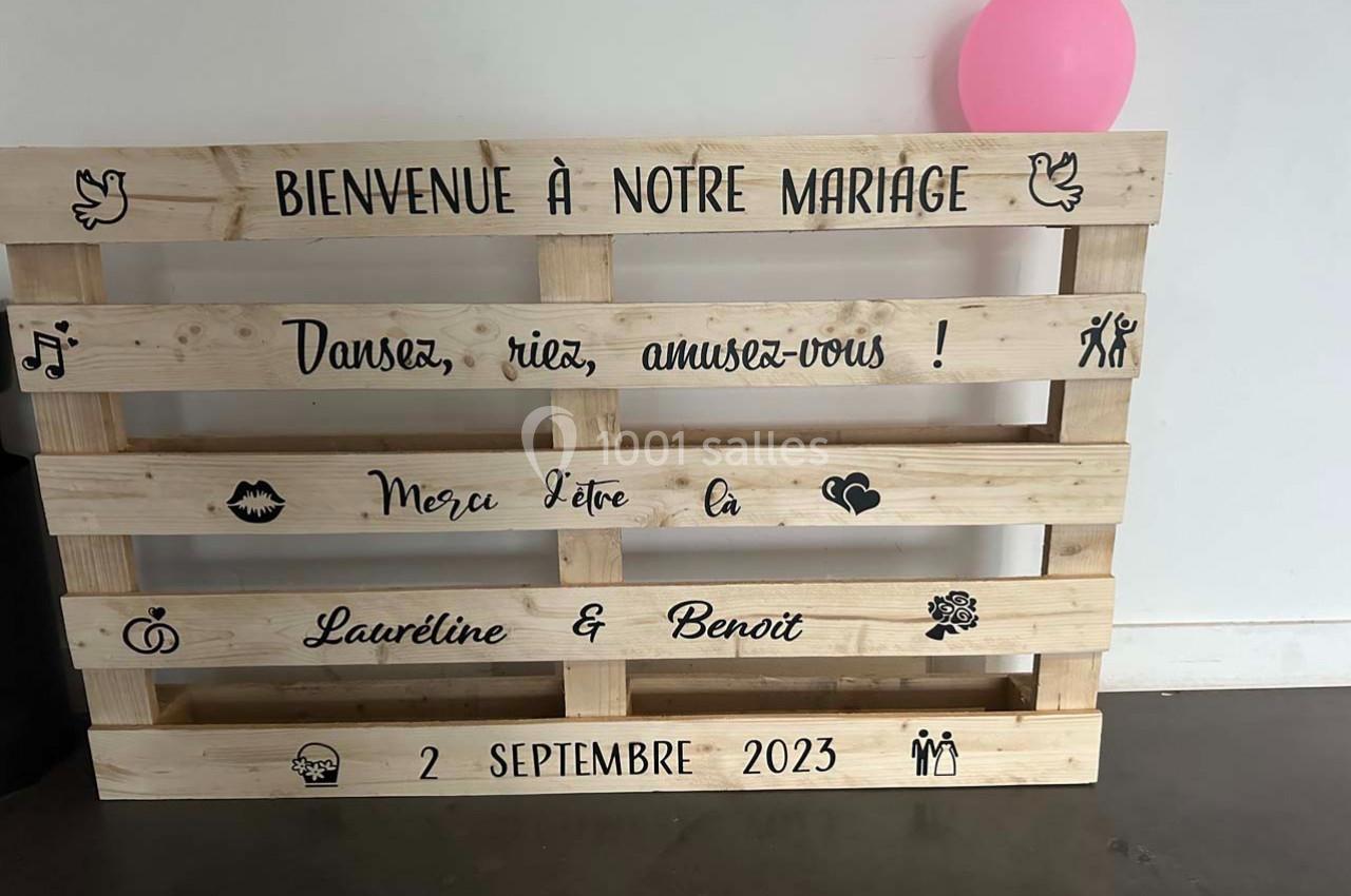 Palette en bois décorée avec des inscriptions pour un mariage, un ballon rose en arrière-plan.