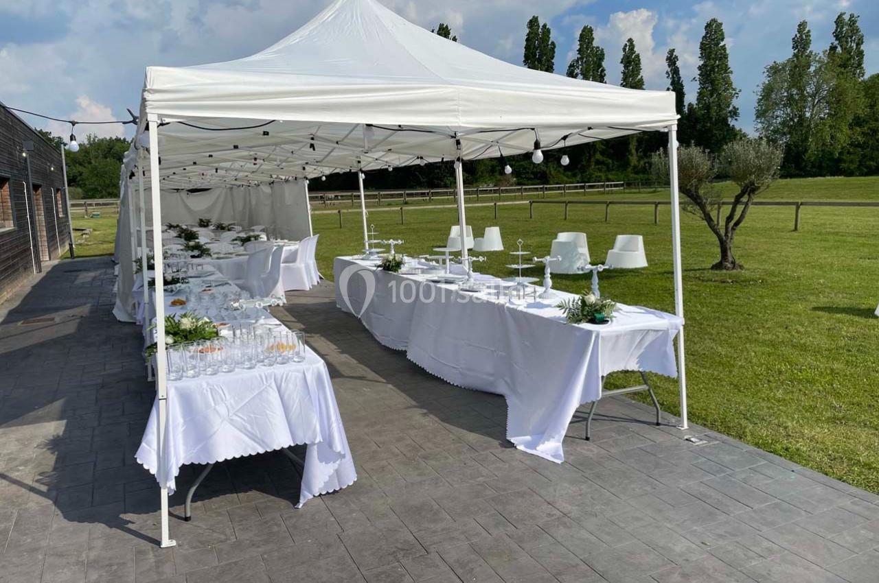 Tente blanche installée en extérieur avec tables dressées pour un événement, entourée d'un espace vert.